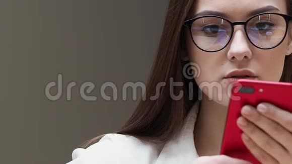 带眼镜的年轻女孩使用智能手机近距离学生手里拿着红色的电话视频的预览图