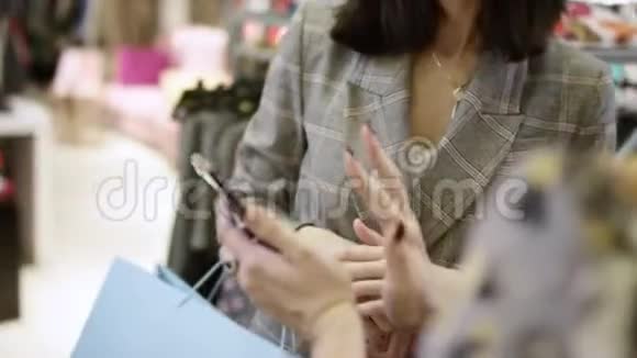 年轻迷人的女人在服装店里互相交谈笑着看着智能手机上的照片视频的预览图