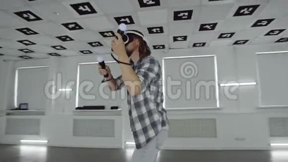 在一个充满白色霓虹灯照明的空玩室里一个穿着vr耳机的年轻人用控制器做跳舞视频游戏视频的预览图