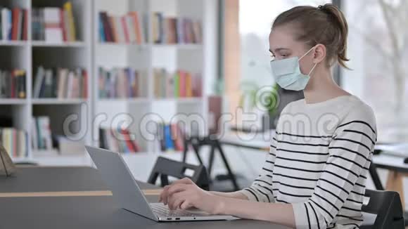 带着口罩的年轻女子在图书馆用笔记本电脑视频的预览图