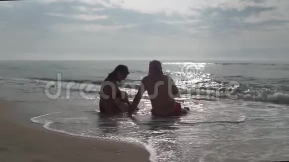 一对夫妇坐在海滩上在日出时用智能手机拍照浪漫夫妇在夏天用智能手机拍照视频的预览图
