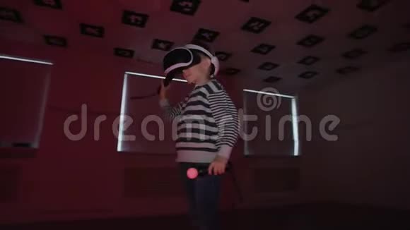 小男孩在虚拟现实中玩得很开心在房间里戴着耳机里面闪烁着霓虹灯着弧线镜头360视频的预览图