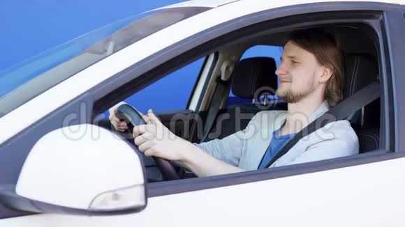布吕内特穿着休闲服的家伙坐在他的车里背景是蓝色的他在挠鼻子年轻人是视频的预览图