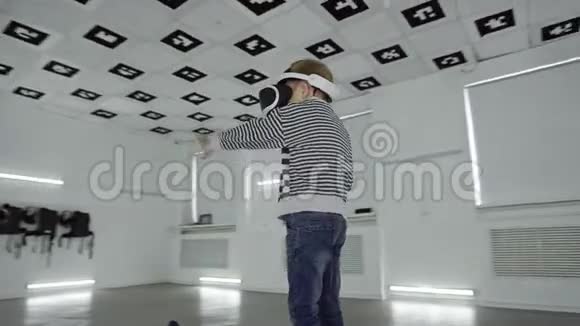 虚拟现实耳机里的小男孩正在一个充满白光的空玩室里挥手追踪弧光射击360视频的预览图
