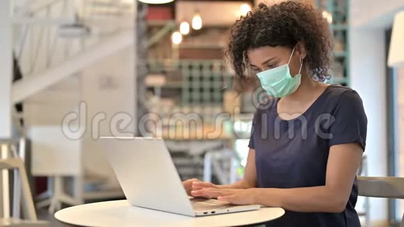 带面罩的非洲青年妇女在咖啡厅使用笔记本电脑视频的预览图