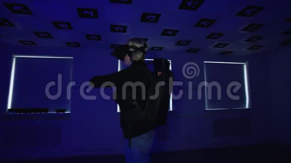 成年女性正在使用带有控制器的虚拟真人耳机玩视频游戏空的游戏室充满了时髦的闪烁视频的预览图
