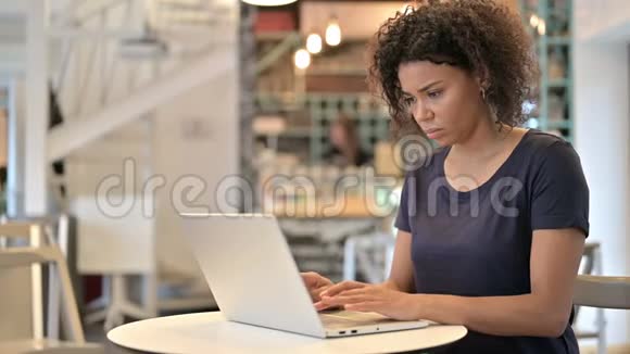 年轻的非洲妇女背部疼痛在咖啡厅使用笔记本电脑视频的预览图