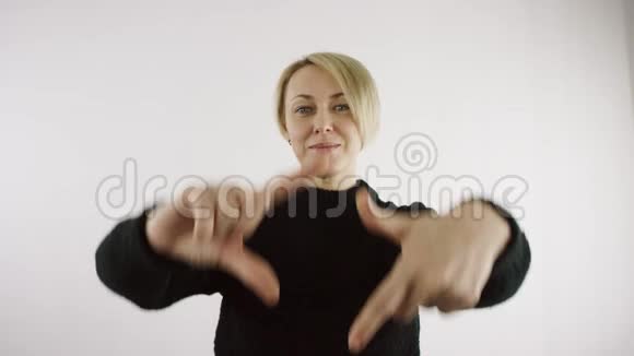 成年白种人白种人金发女人正在明亮的室内用手指在白色背景下做一个框架视频的预览图