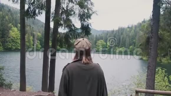 一个穿着雨衣和帽子的女孩走近湖美丽的风景视频的预览图