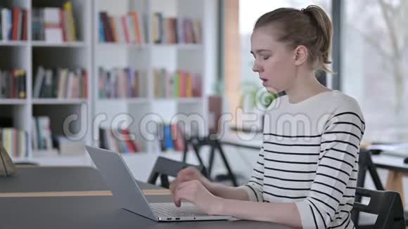 严重的年轻女子使用笔记本电脑在图书馆咳嗽视频的预览图