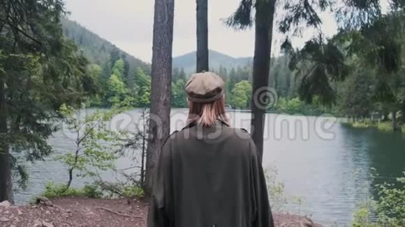 一个穿着雨衣和帽子的女孩走近湖美丽的风景视频的预览图