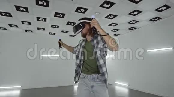 在一个充满白色霓虹灯照明的空玩室里一个穿着vr耳机的年轻人用控制器做游戏视频的预览图
