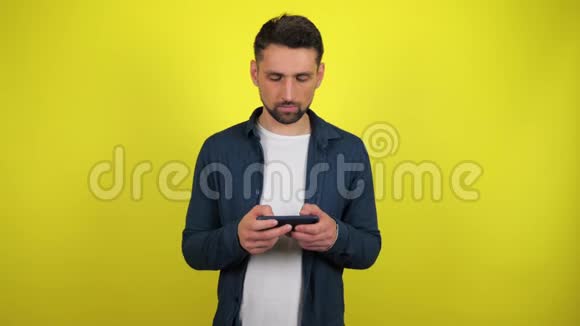 一个穿着蓝色衬衫和白色T恤的年轻人在智能手机上玩游戏输了心烦意乱视频的预览图