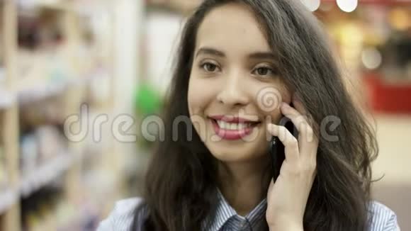 近距离观看漂亮的黑发女孩在电话上交谈开心地微笑着一边选择一边享受谈话视频的预览图