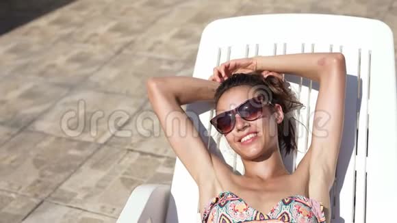 高瞻远瞩的美丽身材白种人比基尼女士身体健康腹部平坦躺在桌椅和日光浴视频的预览图