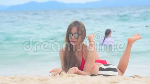 夏天棕褐色的女人在海滩上度假欢快的女人穿着夏装戴着草帽坐在沙滩上眺望大海提姆视频的预览图