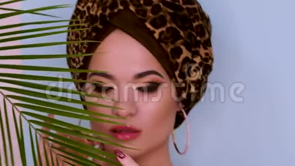 一个漂亮的年轻女子戴着一顶由豹纹织物制成的时尚头巾背景是蓝色视频的预览图