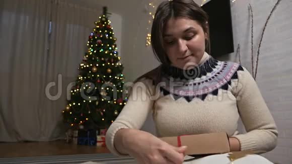 一个年轻女孩把一条丝带系在礼物上一个女人正在包装圣诞礼物视频的预览图