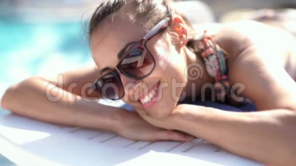 慢动作特写戴墨镜的漂亮白种人女孩躺在桌椅和日光浴的池边视频的预览图
