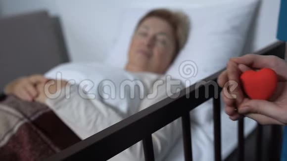 护士手里拿着玩具心在病床上生病的女人的背景善良视频的预览图
