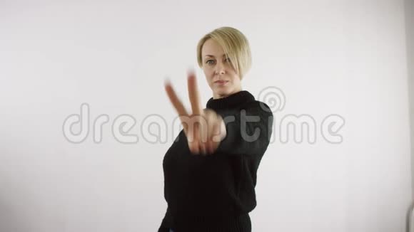 成年白种人金发女子在明亮的室内用两根手指在白色背景下显示v号视频的预览图