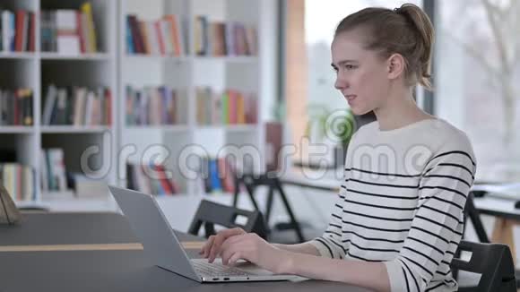 图书馆使用笔记本电脑背疼的年轻女子视频的预览图