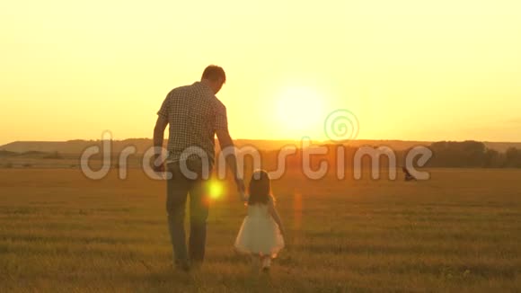 小女儿和她父亲牵着手在草地上散步孩子握着父亲的手家人晚上出去散步视频的预览图