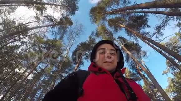 从下面看一个人拿着相机在旋转上面是蓝天还有很高的圣诞树和松树冬季森林TT视频的预览图
