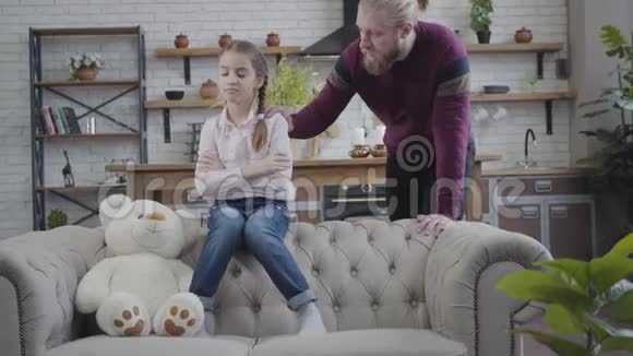 成年英俊的白种人男子牵着女儿肩膀说话可怜的孩子和泰迪熊坐在沙发上视频的预览图
