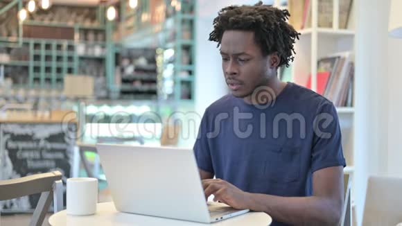 成功的非洲男人在咖啡厅的笔记本电脑上庆祝视频的预览图
