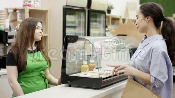 穿着绿色围裙的年轻工作人员为在咖啡店买甜点的顾客服务咖啡师微笑着看着视频的预览图