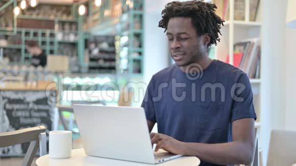 有头痛的非洲男子在咖啡厅的笔记本电脑上工作视频的预览图