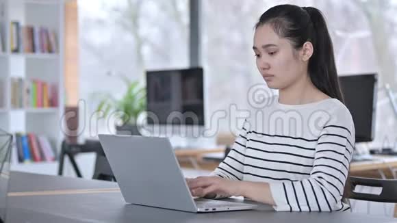 亚洲青年妇女使用笔记本电脑办公室看相机视频的预览图