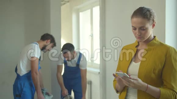 女人在电话里拍照建筑工人在公寓里工作视频的预览图