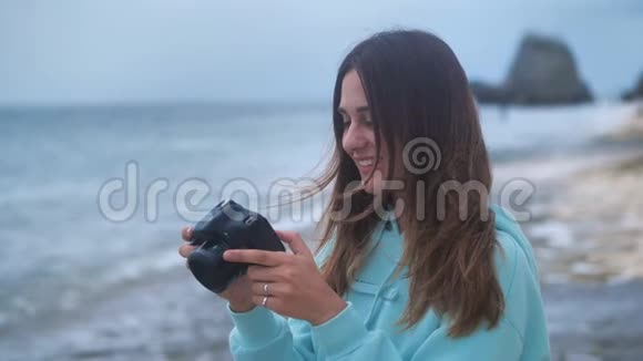 肖像时髦的女人是一个专业摄影师与相机她在黄昏时在海洋背景上拍照4k视频的预览图