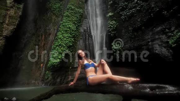美丽的女人穿着泳衣坐在湖边的雨林里瀑布背景下的雨与自然的统一视频的预览图