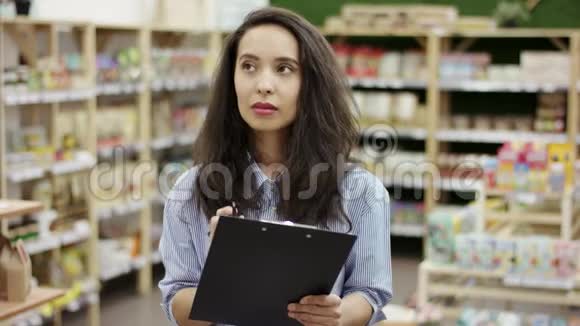 年轻迷人的女士穿着便服手里拿着黑色的文件夹在购物单上点东西做笔记视频的预览图