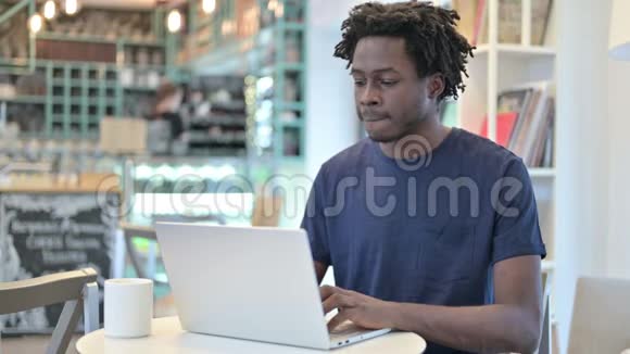 背部疼痛的非洲男子在咖啡厅用笔记本电脑工作视频的预览图