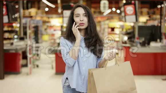 迷人的黑发女孩在电话里交谈微笑友好拿着纸购物袋站在前面视频的预览图