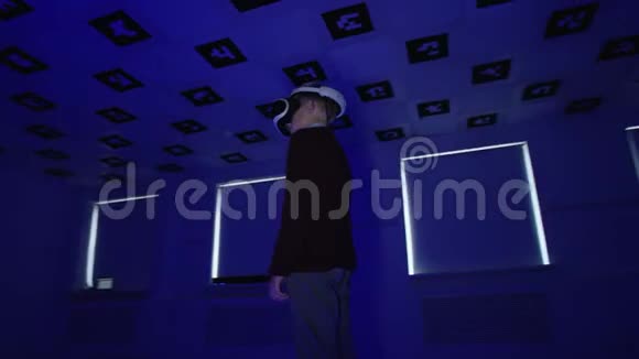 虚拟现实耳机里的男孩正在一个闪烁着红色和蓝色霓虹灯的大房间里环顾四周跟踪弧视频的预览图