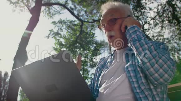 戴眼镜的老人试图在公园里使用电脑但他不能他打电话给能帮他的人视频的预览图