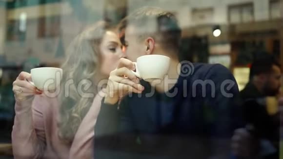 年轻的浪漫情侣坐在咖啡厅的窗前拥抱亲吻和喝咖啡视频的预览图