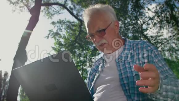 戴眼镜的老人试图在公园里使用电脑但他不了他打电话给能帮他的人视频的预览图