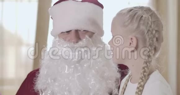 可爱的金发白种人女孩扎着辫子在圣诞老人耳边低语在家里和圣诞老人说话的漂亮孩子视频的预览图