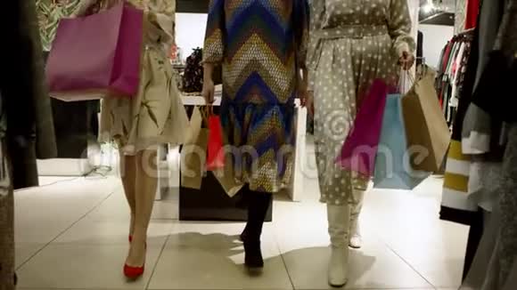 近距离拍摄了三个快乐的女人拿着购物袋和谈话走出服装店视频的预览图