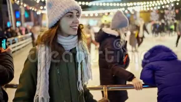快乐微笑的年轻女子穿着温暖的冬衣站在城市溜冰场的背景下视频的预览图