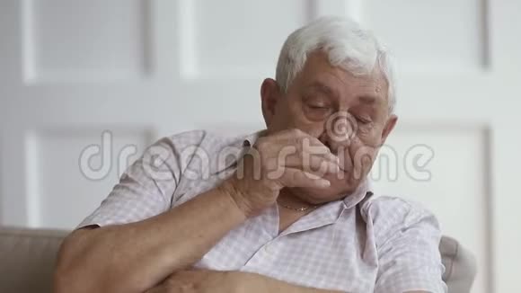 悲伤的灰发老人独自坐在家里哭泣视频的预览图