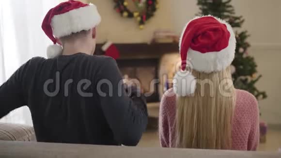 成人白种人男子伸展和把手放在妇女肩膀的后视图戴着新年帽子的夫妇视频的预览图