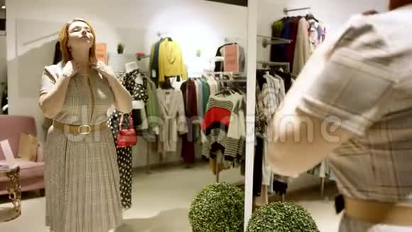 漂亮的中年短发女人正在商场的服装店里对着镜子穿一件衣服视频的预览图