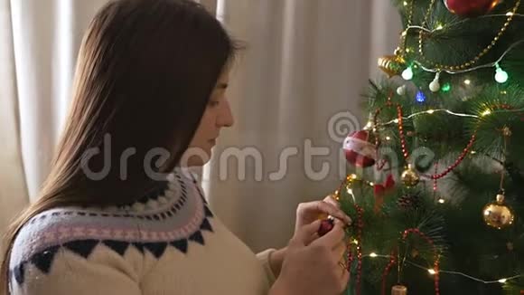 穿毛衣的漂亮女孩用球装饰圣诞树美丽的圣诞室视频的预览图